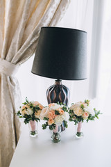 Three wedding bouquets of pink flowers stand on white table before black lamp