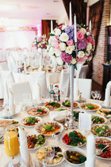 Centerpiece made of white candles and flowers stands on the middle of dinner table