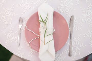 Green branch, white serviette and pearls on pink dinner plate