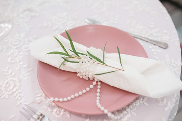 Green branch, white serviette and pearls on pink dinner plate