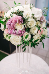 Centerpiece made of stunning white roses and pink hydrangeas stands on a little round dinner table