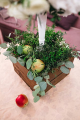 Wooden box with apples and greenery stands on the dinner table