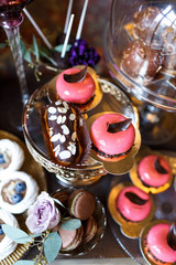 Dishes with cookies, eclairs, macaroons and other sweets made of chocolate and cream served on black table