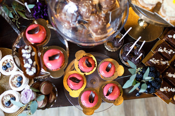 Dishes with cookies, eclairs, macaroons and other sweets made of chocolate and cream served on black table