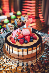 Delicious chocolate berry cake decorated with pink macaroons stands on the golden table