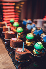 Dishes with cookies, eclairs, macaroons and other sweets made of chocolate and cream served on black table