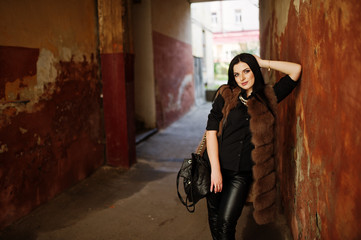 Fashion outdoor photo of gorgeous sensual woman with dark hair in elegant clothes and luxurious fur coat at old street with grunge walls.