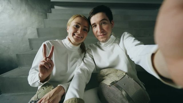 POV of Two young smiling fencers man and woman taking selfie on smartphone camera after fencing training indoors