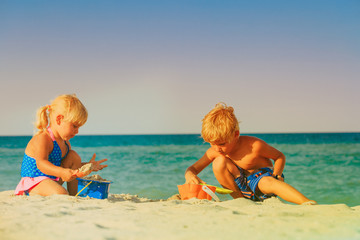 Naklejka premium little boy and girl play with sand on beach