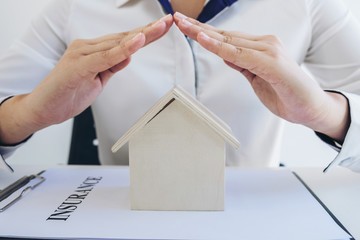 insurance and care protection of house concept, woman with protective gesture of small home model