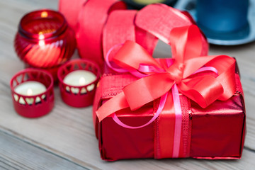 Red gift box with ribbon, decorated with candles on a wooden background.