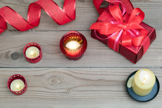 Red gift box with ribbon, decorated with candles on a wooden background.