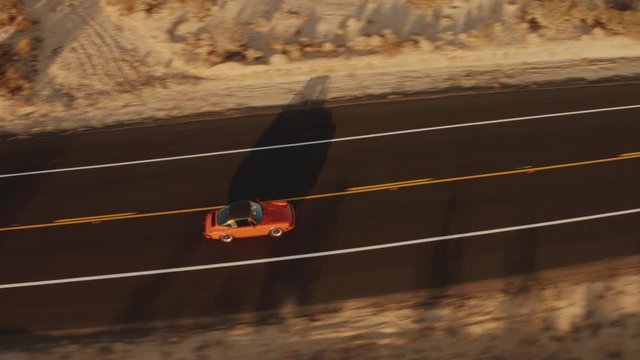 Aerial View Red Classic Car Driving Along Desolate Desert Road At Sunset