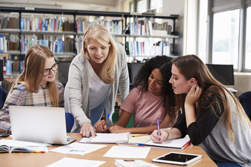 Woman Teacher Working With Female College Students In Library