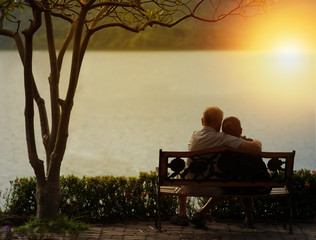 Older silhouette with love in couple resting on a bench in the park.