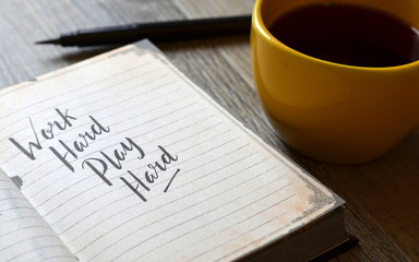 WORK HARD PLAY HARD hand-lettered in notebook on desk with cup of coffee