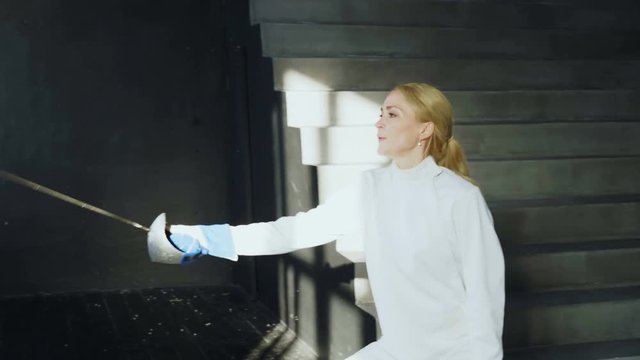 Young concentrated fencer woman training fencing exercise in studio indoors