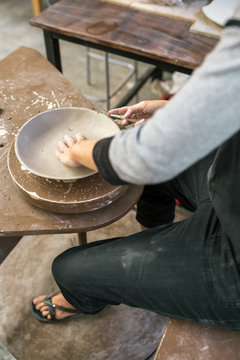Crop artisan shaping clay plate with instrument
