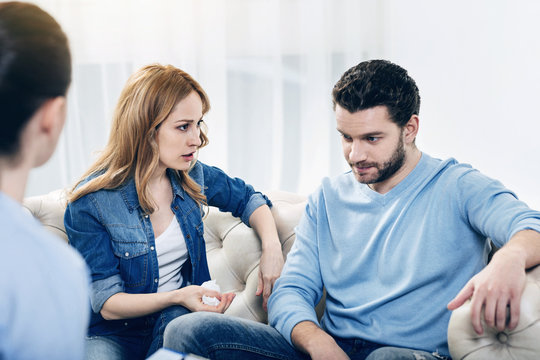 Discussion of problems. Unhappy sad young woman looking at her husband and talking to him while having a therapeutic session