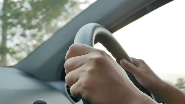 Closeup of female teen driver's hands on steering wheel in evening. Alone person driving in the country in twilight, slowmotion shot.