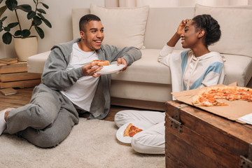 couple eating pizza beside sofa