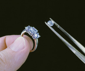 hand with diamond in tweezers placing on ring