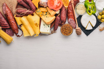 Assorted cheeses and traditional sausages and vegetables on a white wooden background. Cheese brie,...