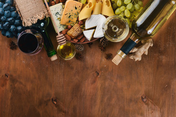 Fototapeta premium A bottle of wine, and a large assortment of cheeses, honey, nuts and spices, on a wooden table. Top view. Free space for text.