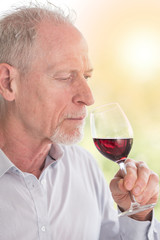 Mature man tasting red wine, light effect