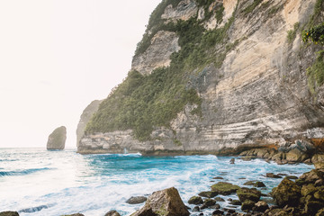 Tropical blue ocean with waves and rocky cliff in Bali. Rocks and sea