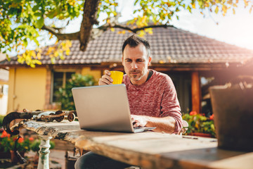 Men drinking coffee and using laptop at backyard patio