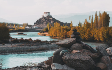 Fototapeta na wymiar Stone stupa foreground with Stakna Gompa and Indus river before sunset with cloudy sky and mountains background