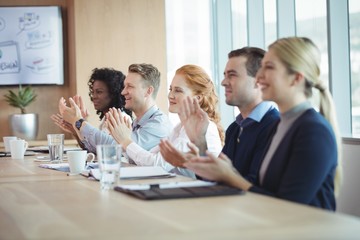 Happy business people clapping at conference table during