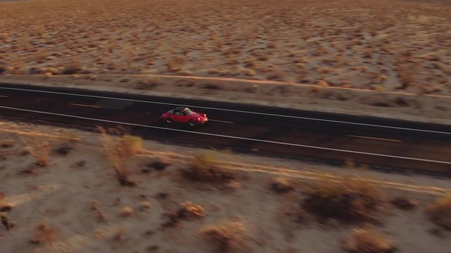 Aerial View Red Classic Car Driving Along Desolate Desert Road At Sunset