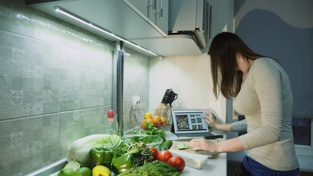 Woman checks recipe on digital tablet before adding tomatoes to a glass bowl for salad