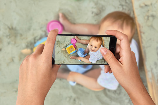 Closeup hand holding phone shooting Beautiful baby playing in the sandbox