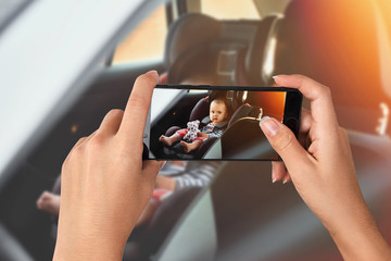 Closeup hand holding phone shooting Adorable baby in safety car seat.