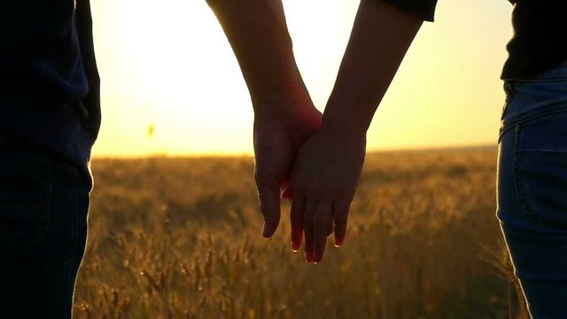 Couple holding hands on a golden wheat field over a beautiful sunset. Slow motion.