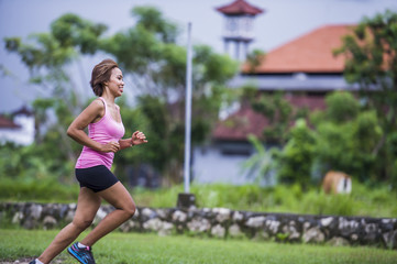 young attractive Asian sport runner woman running in the jungle smiling happy in training workout on herb background in fitness