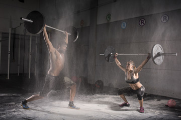 Motivational wide shot of young man and woman holding barbells overhead