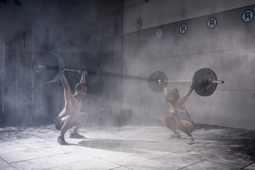 Motivational wide shot of young man and woman holding barbells overhead