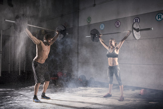 Motivational Wide Shot Of Young Man And Woman Holding Barbells Overhead