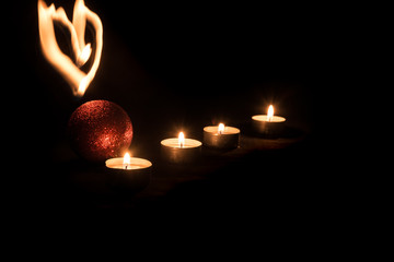 burning candle, christmas ball and light heart in front of black background
