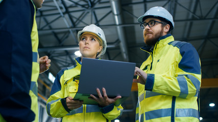 Male and Female Industrial Engineers Talk with Factory Worker while Using Laptop. They Work at the Heavy Industry Manufacturing Facility. Low Angle Shot.