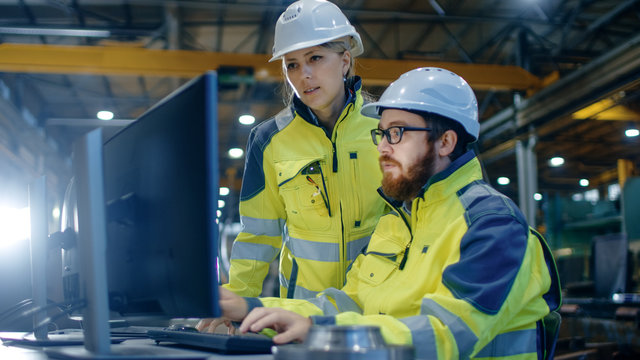 Male Industrial Engineer Works on the Personal Computer while Female Manager Talks about Project. They Work in Heavy Industry Manufacturing Factory.