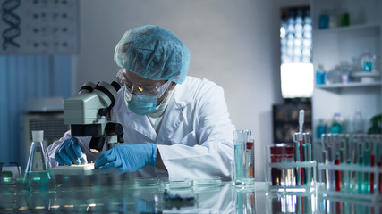 Medical lab worker examining laboratory glass with sample through microscope