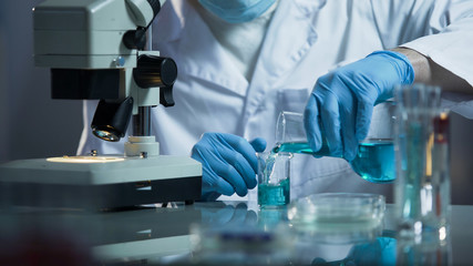 Lab assistant pouring liquid reagent into beaker to create chemical solution