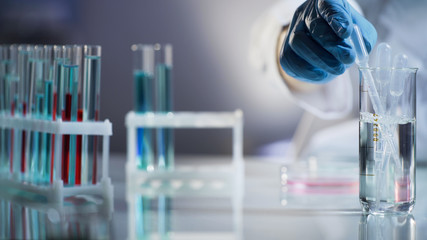 Laboratory assistant putting pipette into sterile mixture after conducting tests