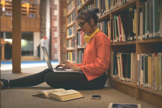 Girl using laptop in library - Powered by Adobe