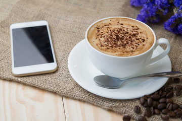 Close up a cup of hot coffee on wood table with smartphone and coffee beans.